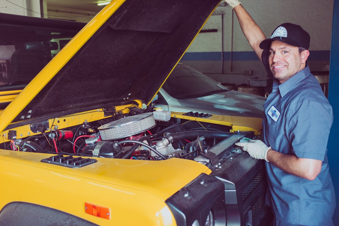 Mecânico sorrindo ao lado do motor de um carro com o capô aberto
